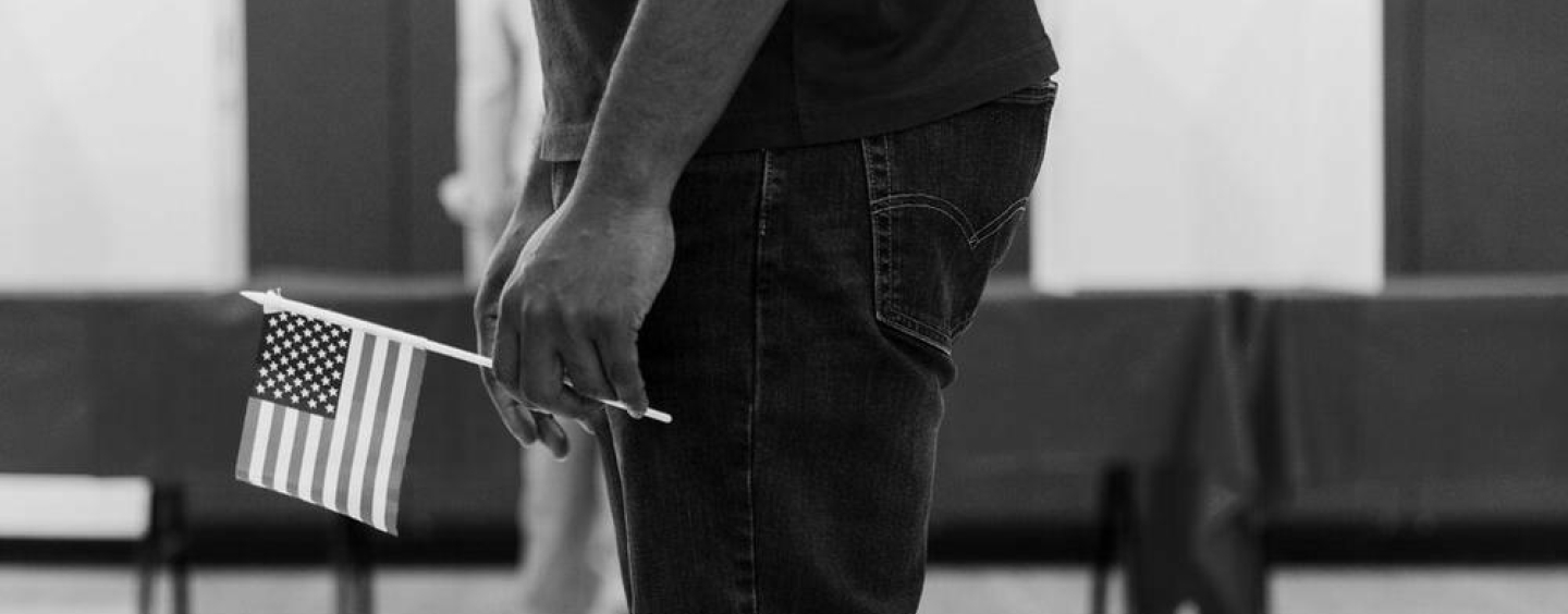 male body holding a small american flag black and white