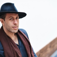 white man wearing black clothes, black fedora, and brown scarf