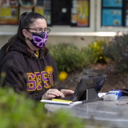 Student outside with mask on working on computer